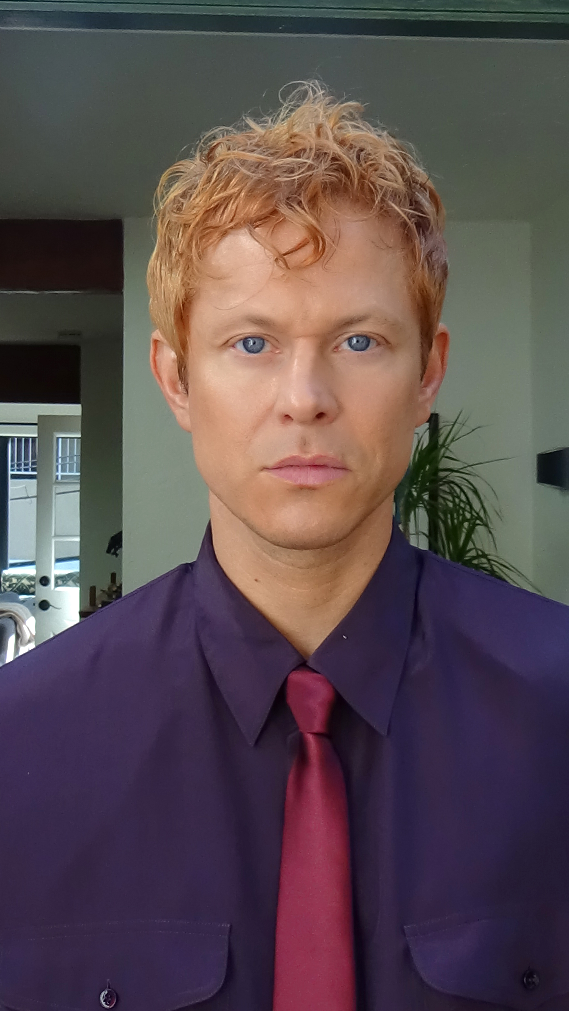 Close up portrait of Mike Hadreas making eye contact with the camera in a purple button up shirt and maroon tie